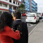 Estudiantes con mochilas caminan junto a una calle y edificios.