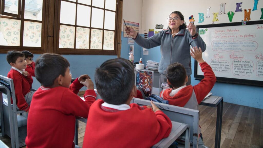 Docente conversa con estudiantes que levantan la mano en un aula.