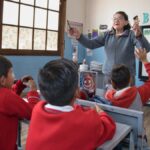 Docente conversa con estudiantes que levantan la mano en un aula.
