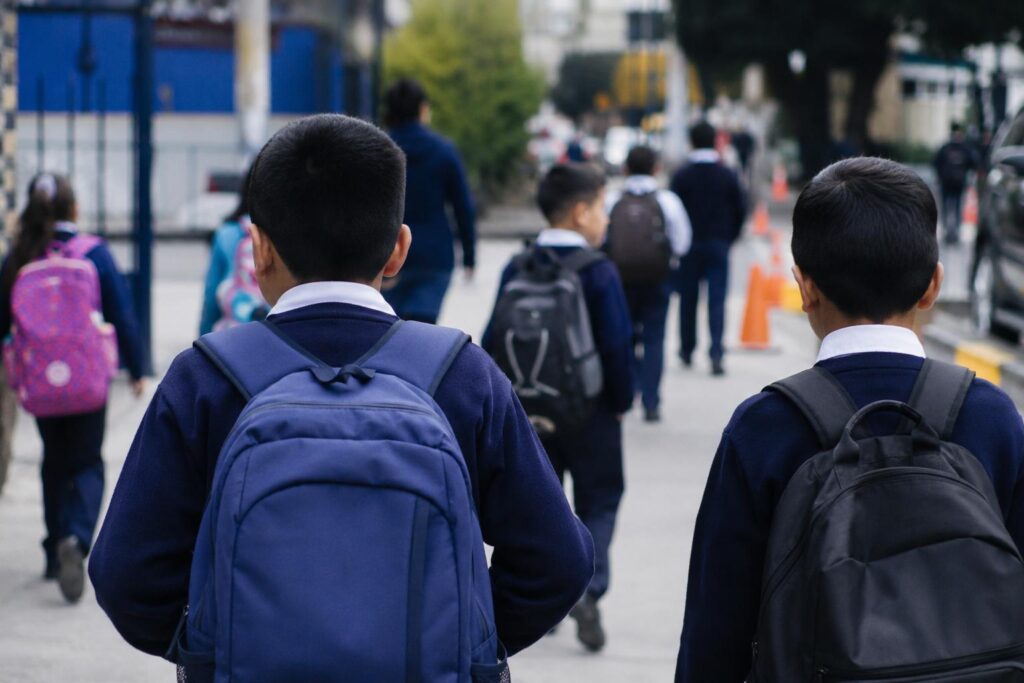 Estudiantes con mochilas caminan hacia un establecimiento educativo.