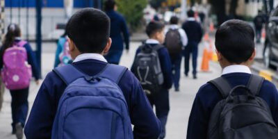 Estudiantes con mochilas caminan hacia un establecimiento educativo.
