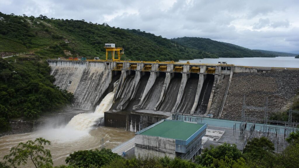 Represa con vertederos y agua que fluye junto a laderas con vegetación.