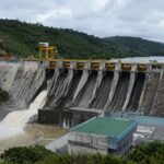 Represa con vertederos y agua que fluye junto a laderas con vegetación.