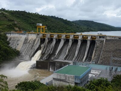 Represa con vertederos y agua que fluye junto a laderas con vegetación.