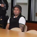 Daniel Salcedo sentado junto a un agente uniformado en una sala.