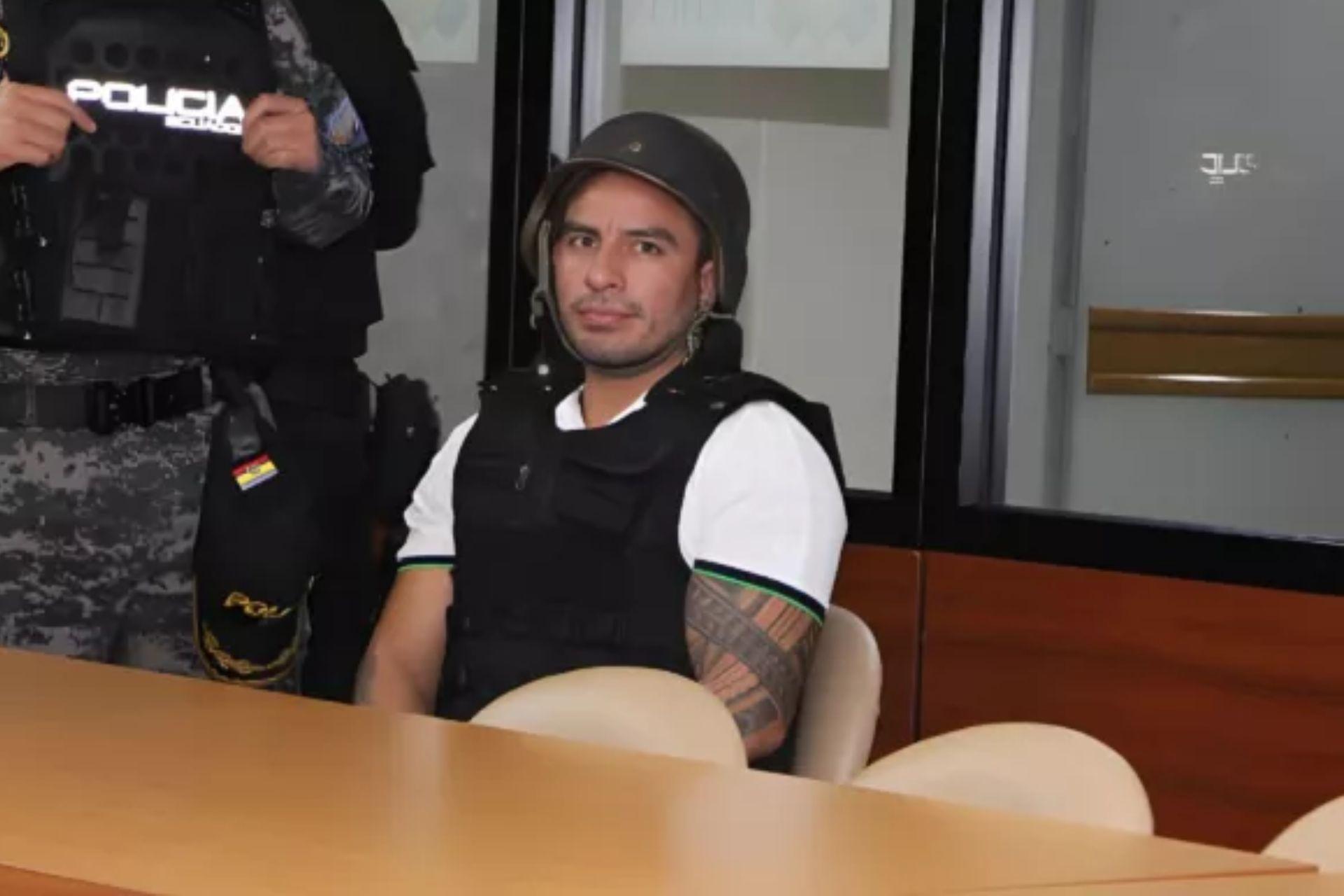 Daniel Salcedo sentado junto a un agente uniformado en una sala.