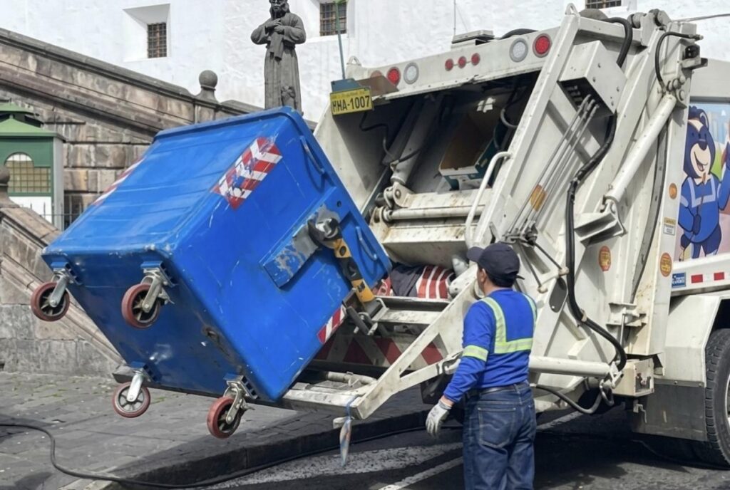 Trabajador opera un camión recolector para vaciar un contenedor de residuos.