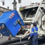 Trabajador opera un camión recolector para vaciar un contenedor de residuos.
