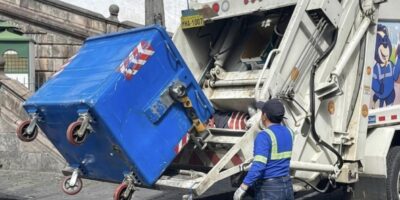 Trabajador opera un camión recolector para vaciar un contenedor de residuos.