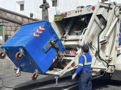 Trabajador opera un camión recolector para vaciar un contenedor de residuos.