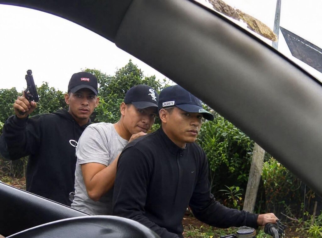 Hombre acompañado por agentes durante un procedimiento junto a un vehículo.