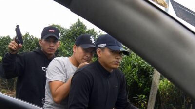 Hombre acompañado por agentes durante un procedimiento junto a un vehículo.