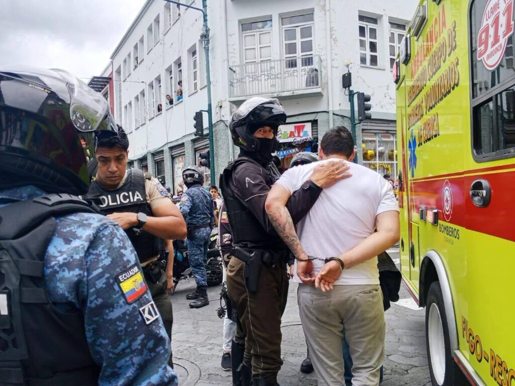 Agentes policiales acompañan a un hombre junto a un vehículo de emergencias.