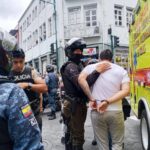 Agentes policiales acompañan a un hombre junto a un vehículo de emergencias.