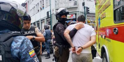 Agentes policiales acompañan a un hombre junto a un vehículo de emergencias.