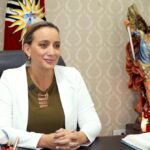 Johana Núñez sentada en una oficina con una bandera ecuatoriana al fondo.