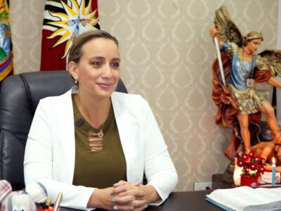 Johana Núñez sentada en una oficina con una bandera ecuatoriana al fondo.