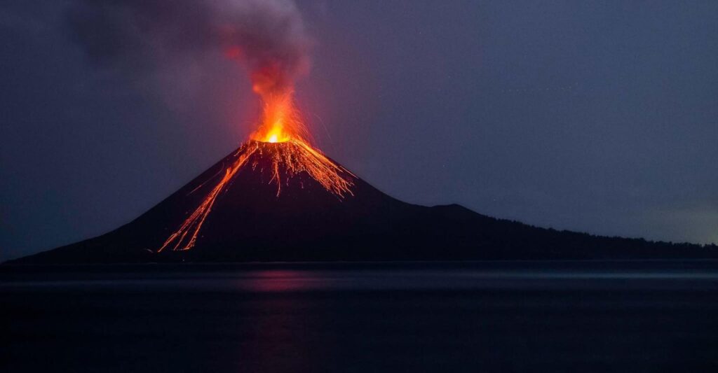 Volcán en erupción con lava y una columna de humo durante la noche.