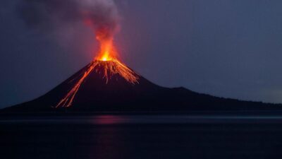 Volcán en erupción con lava y una columna de humo durante la noche.