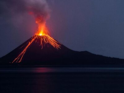 Volcán en erupción con lava y una columna de humo durante la noche.