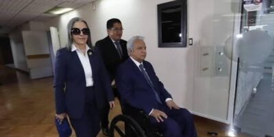 Lenín Moreno en silla de ruedas acompañado por personas en un edificio.