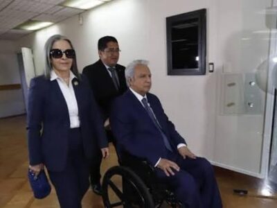 Lenín Moreno en silla de ruedas acompañado por personas en un edificio.