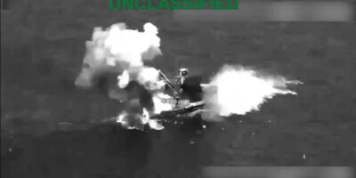 Captura aérea en blanco y negro de una embarcación envuelta en humo y llamas.