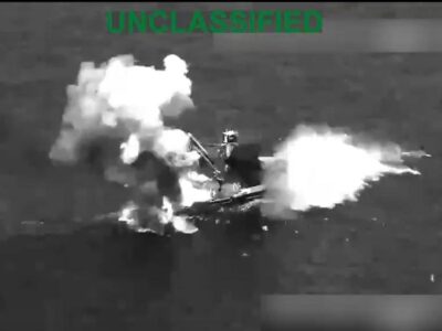 Captura aérea en blanco y negro de una embarcación envuelta en humo y llamas.