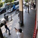 Captura de cámara de seguridad de personas en una acera junto a una calle.
