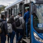Pasajeros suben a un autobús azul en una parada de transporte público.