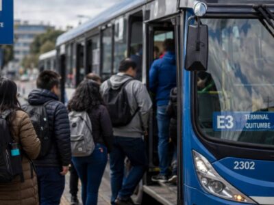 Pasajeros suben a un autobús azul en una parada de transporte público.