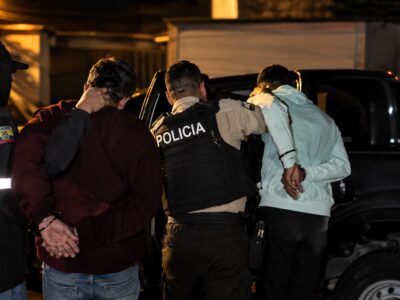 Agentes de Policía junto a dos hombres con las manos detrás de la espalda durante un operativo nocturno.