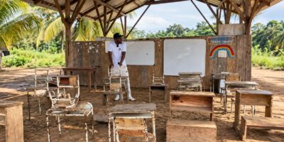 Estudiantes y pupitres en un aula rural con techo de madera y paredes abiertas.