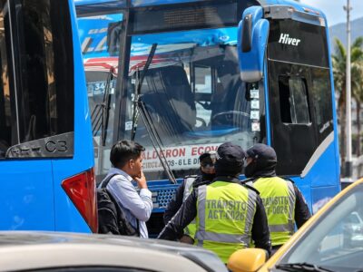 Agentes municipales y otras personas junto a la puerta de un autobús azul.