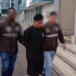 Dos agentes acompañan a un hombre frente a un edificio; los rostros de los agentes están difuminados.
