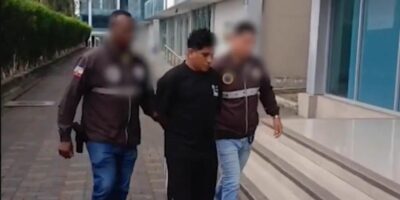 Dos agentes acompañan a un hombre frente a un edificio; los rostros de los agentes están difuminados.