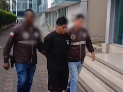 Dos agentes acompañan a un hombre frente a un edificio; los rostros de los agentes están difuminados.