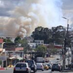 Una columna de humo se eleva detrás de viviendas y una calle con vehículos.