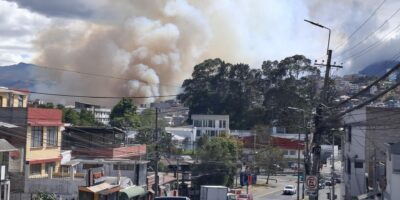 Una columna de humo se eleva detrás de viviendas y una calle con vehículos.