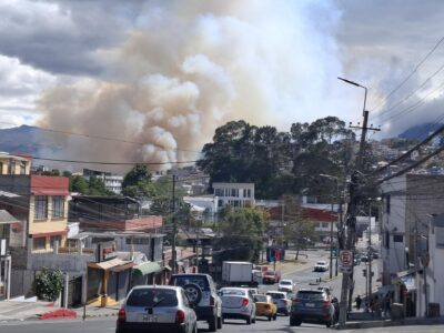 Una columna de humo se eleva detrás de viviendas y una calle con vehículos.