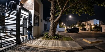 Entrada de una urbanización y una acera iluminadas durante la noche.