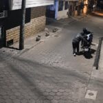 Captura de una cámara de seguridad con personas junto a una motocicleta en una acera durante la noche.