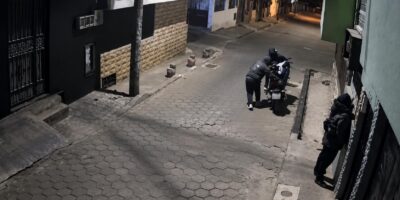 Captura de una cámara de seguridad con personas junto a una motocicleta en una acera durante la noche.