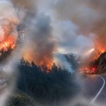Incendio y humo en una ladera junto a una vía y edificios.