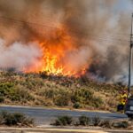 Llamas y humo sobre una ladera junto a una vía con vehículos.