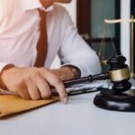 Imagen ilustrativa de una persona ante documentos, un mazo judicial y una balanza.