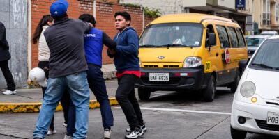 Dos hombres y un agente de tránsito en una calle con vehículos.
