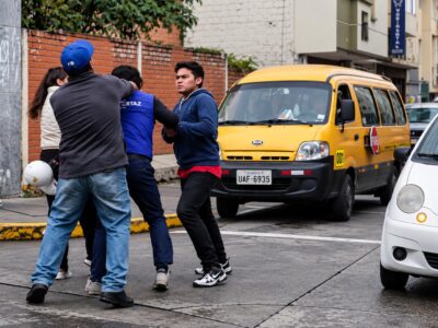 Dos hombres y un agente de tránsito en una calle con vehículos.