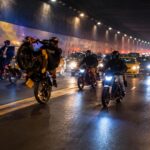 Motociclistas y otros vehículos dentro de un túnel iluminado durante la noche.
