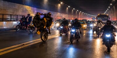 Motociclistas y otros vehículos dentro de un túnel iluminado durante la noche.